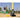 A robotic tennis ball launcher shoots balls on a court with a player swinging a bat in the background