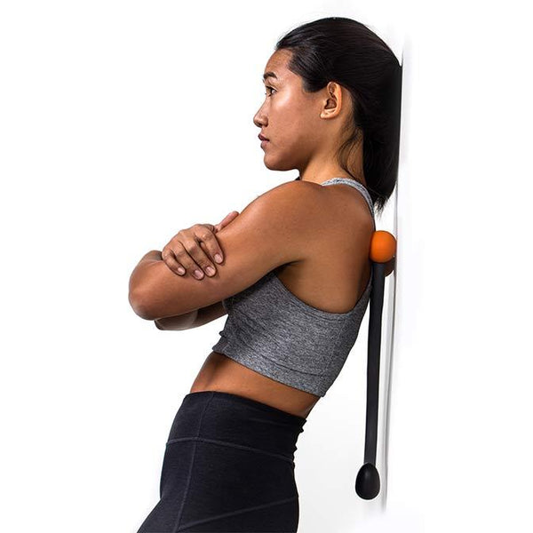 A woman uses the TriggerPoint AcuCurve Cane Massage Tool against a wall to release tight muscles surrounding her spine.